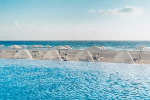 Beach cabanas with white dome structures and umbrellas along turquoise ocean waters