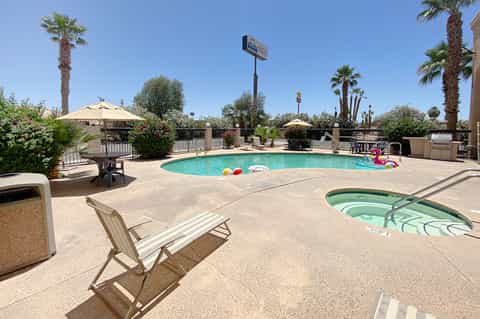 Resort pool with turquoise water, palm trees, beige umbrellas, and lounge chairs on sunny day