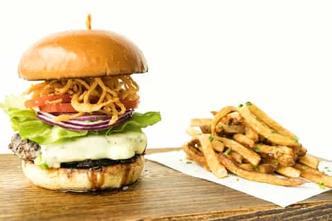 Gourmet burger with melted cheese, crispy fries, lettuce, and tomato on wooden serving board