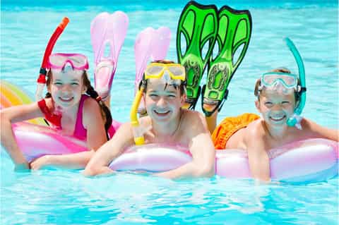 Three children in swimming pool wearing colorful snorkel gear and holding inflatable pool floats