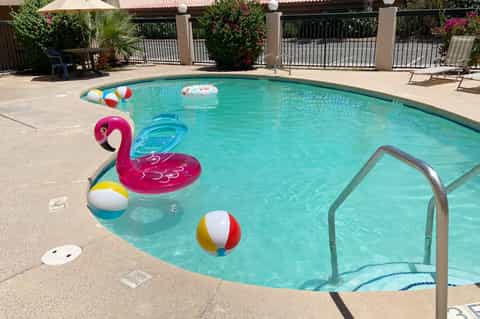 Resort pool with colorful floats, lounge chairs, and white umbrellas by building