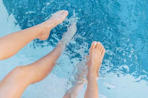 Person's legs submerged in bright blue swimming pool water from overhead perspective