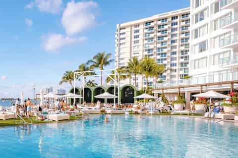 Luxury resort pool with lounge chairs, white cabanas, and waterfront high-rise building