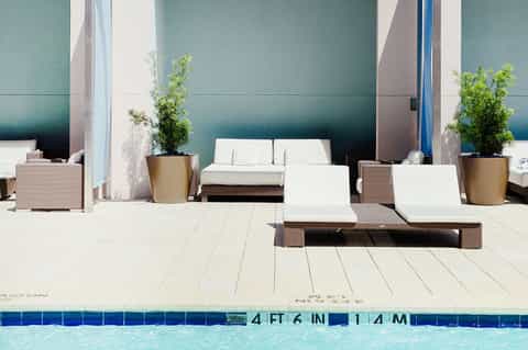 Minimalist pool deck with modern lounge chairs, potted plants, and teal accent wall