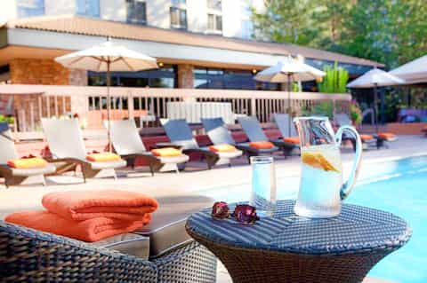 Poolside lounge area with orange towel, water pitcher, sunglasses, and lounge chairs with umbrellas