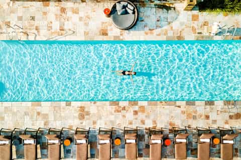 Aerial view of person swimming in narrow lap pool with tiled deck and lounge chairs