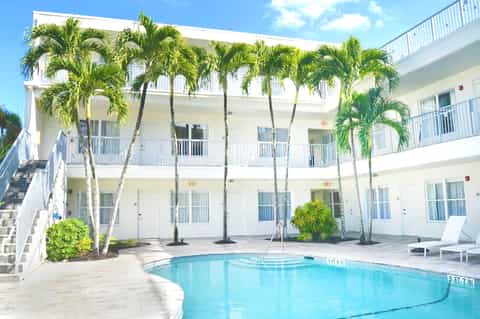 White multi-story beachfront hotel with palm trees and curved swimming pool on sandy beach