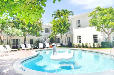 Resort courtyard with white buildings, pool, lounge chairs, and palm trees
