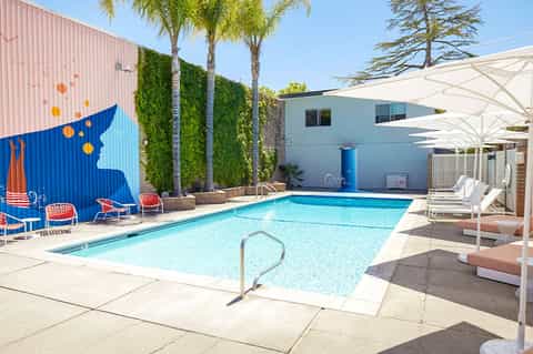 Vintage-style pool with retro metal lounge chairs, white umbrellas, and bold blue mural on corrugated wall