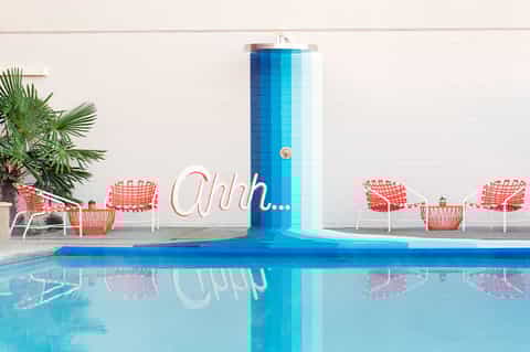 Pool area with blue water feature, red chairs, and palm tree backdrop