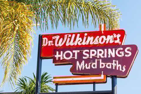 Vintage red neon sign for Dr. Wilkinson's Hot Springs and Mud Baths under palm trees