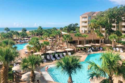 Beachfront resort with multiple pools, palm trees, and multi-story accommodation buildings overlooking the ocean