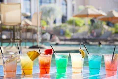 Colorful cocktails lined up at pool bar with citrus garnishes and black straws