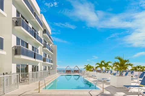 Modern beachfront resort with infinity pool, palm trees, lounge chairs, and ocean views under blue sky