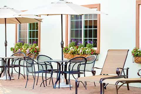 Beachfront patio with white umbrellas, lounge chairs, flowering planters, and ocean view