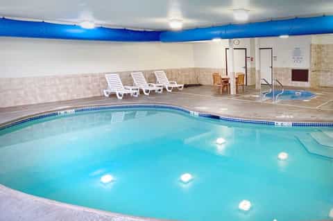 Indoor heated pool with lounge chairs in a bright facility featuring blue ceiling elements
