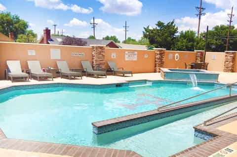 Bright turquoise swimming pool with spa jets and lounge chairs against tan accent wall