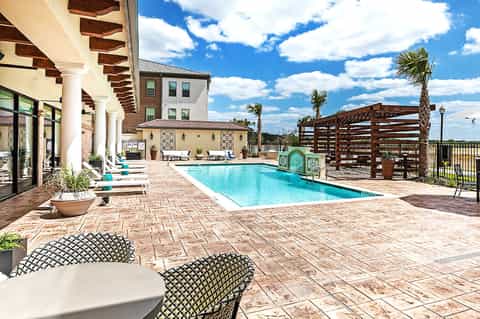 Resort pool deck with lounge chairs, pergola shade structures, and main building with arches