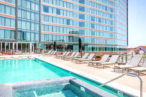 Outdoor pool with lounge chairs in front of modern glass hotel building on sunny day