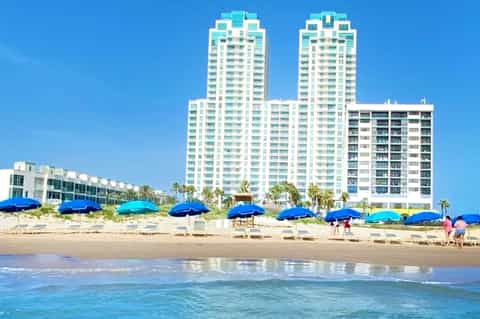 Beachfront resort high-rise towers with blue umbrellas lining sandy beach and turquoise ocean waves