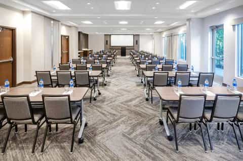 Conference room with classroom-style seating, projection screen, and large windows with natural light