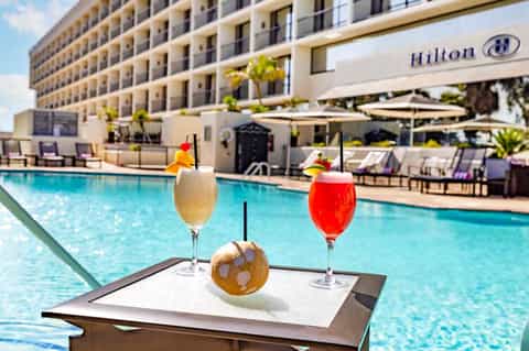 Hilton hotel poolside with tropical cocktails, resort building, lounge chairs, and umbrella shade