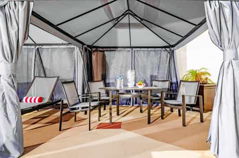 Beach cabana tent with white curtains, lounge chairs, table, and palm tree decoration