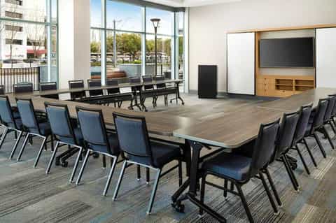Modern conference room with long dark table, blue chairs, large windows overlooking outdoor area