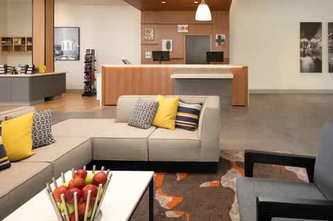 Modern hotel lobby with gray seating area, wooden reception desk, and yellow accent pillows