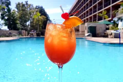 Tropical cocktail by pool with colorful garnish and resort background