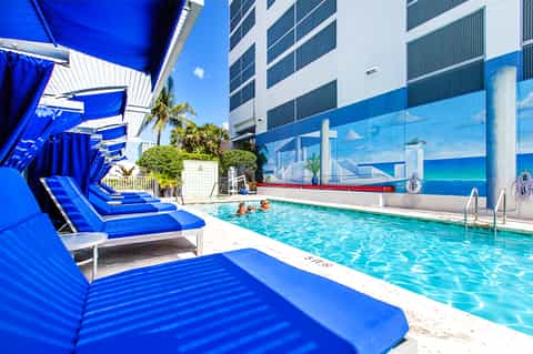Beachfront hotel pool with blue lounge chairs, palm trees, and ocean view