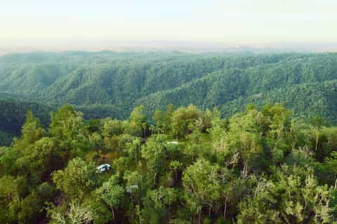 Aerial view of lush green forested hills and valleys with white vehicle visible on a road