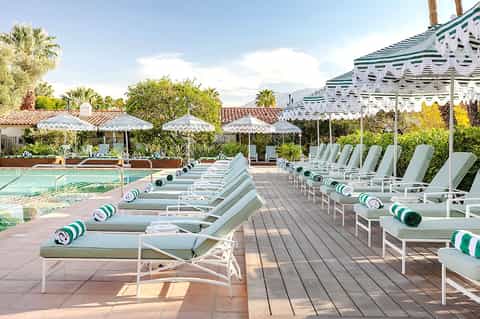 Resort pool deck with white lounge chairs, green and white striped umbrellas, pergolas, and mountain backdrop