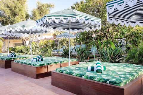 Pool loungers with tropical leaf pattern under striped umbrellas and wooden pergola