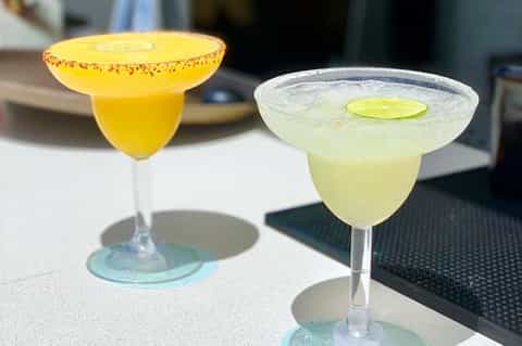 Two colorful cocktails with garnishes on white surface - yellow margarita and lime drink