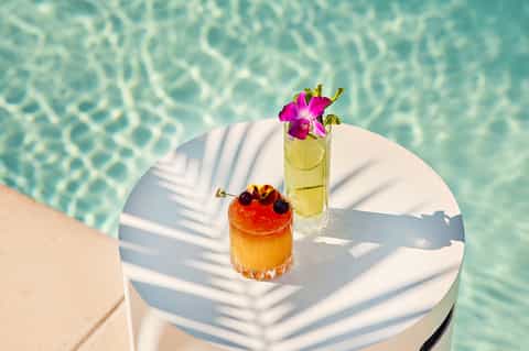 Tropical cocktails with flowers on a white table beside a turquoise pool