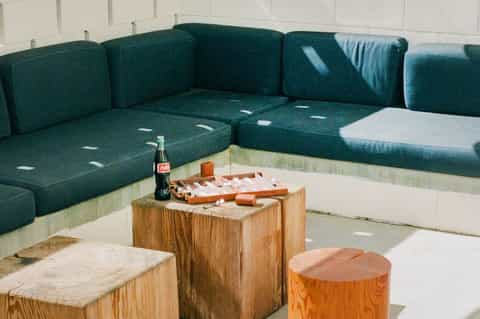 Outdoor lounge area with teal cushioned seating around wooden tables on concrete patio