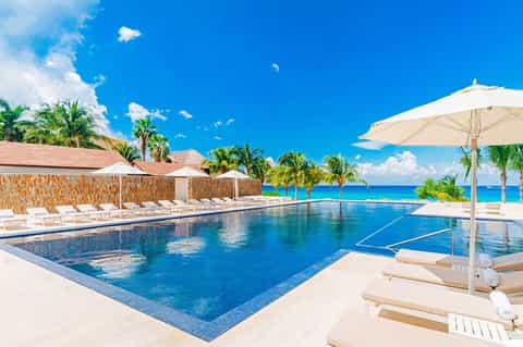 Luxury beachfront pool with turquoise water, white loungers, umbrellas, and ocean view