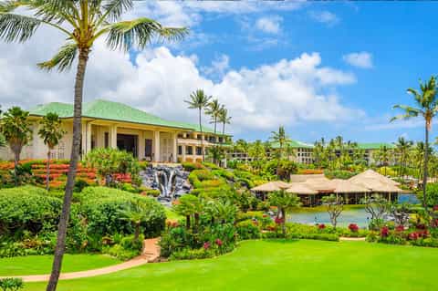 Luxury resort grounds with manicured lawns, flowering gardens, palm trees, and yellow main building with green roof