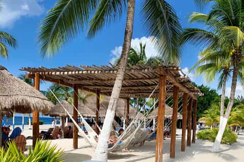 Beach cabana with wooden pergola, hammocks, and palm trees overlooking ocean