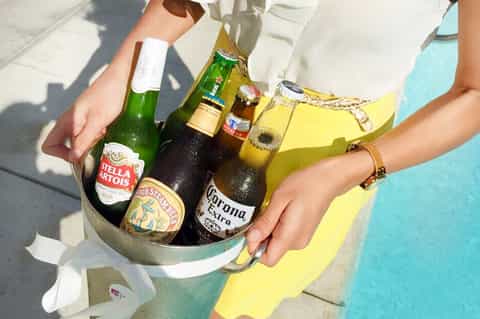 Hand holding ice bucket with beer bottles by turquoise pool water