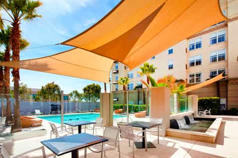 Resort courtyard pool with orange shade sails, palm trees, and modern apartment building