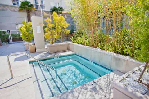 Jacuzzi spa pool in courtyard with bamboo plants, modern building, and sunny patio