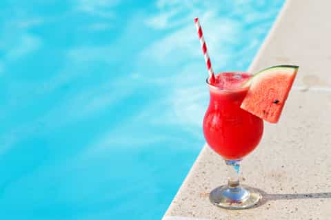 Red watermelon cocktail with striped straw and fresh watermelon slice by pool