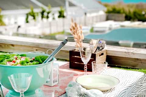 Poolside dining setup with salad bowl, glassware, and ocean view in background
