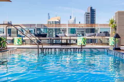 Olympic-sized rooftop swimming pool with city skyline and lounge seating in background