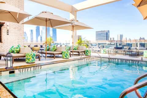 Rooftop pool with lounge chairs, umbrellas, and city skyline backdrop