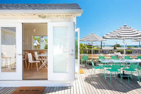 Beachfront resort deck with white building, striped umbrellas, and green lounge chairs