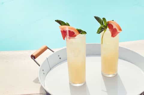 Two grapefruit-garnished mocktails with mint on white poolside table overlooking turquoise water