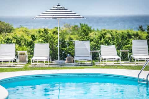 Resort pool area with white loungers, striped umbrella, and ocean view